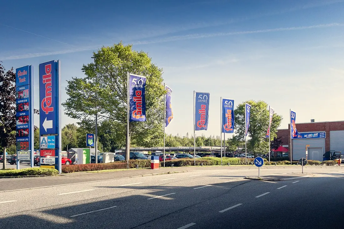 Ortsaufnahme (Veranstaltungsort, ohne Markt): Einfahrt und Parkplatz des famila-Markts in Kiel-Neumeimersdorf mit Fahnen – ohne Flohmarkt